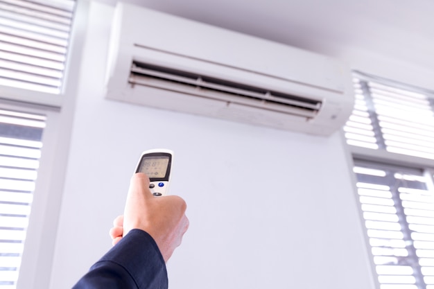 Ar condicionado com controle remoto, dentro da sala com o homem operando o controle remoto.