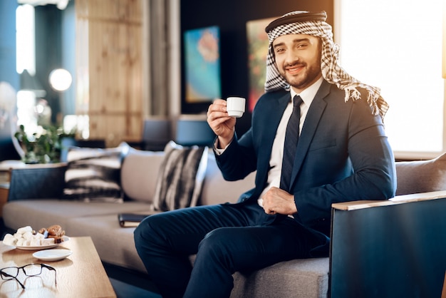Arab trinkt Kaffee auf der Couch im Hotelzimmer.