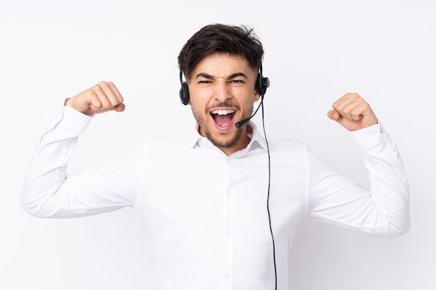 Árabe do telemarketing trabalhando com um fone de ouvido isolado no branco comemorando uma vitória