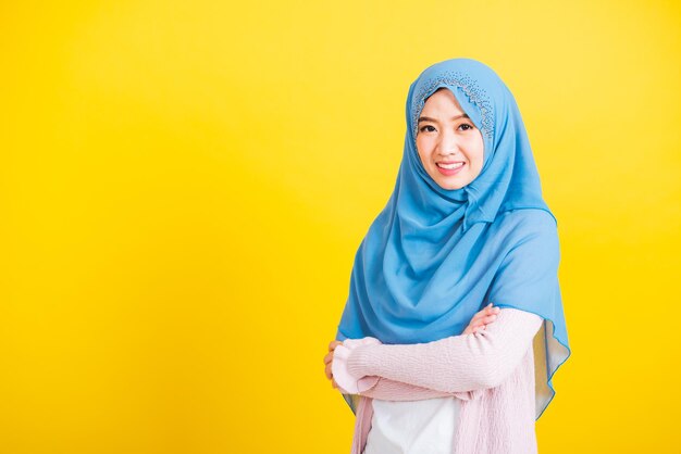 Árabe musulmán asiático, Retrato de una joven feliz y hermosa religiosa islámica usa velo hijab ella sonríe con el brazo cruzado, foto de estudio aislada en un fondo amarillo