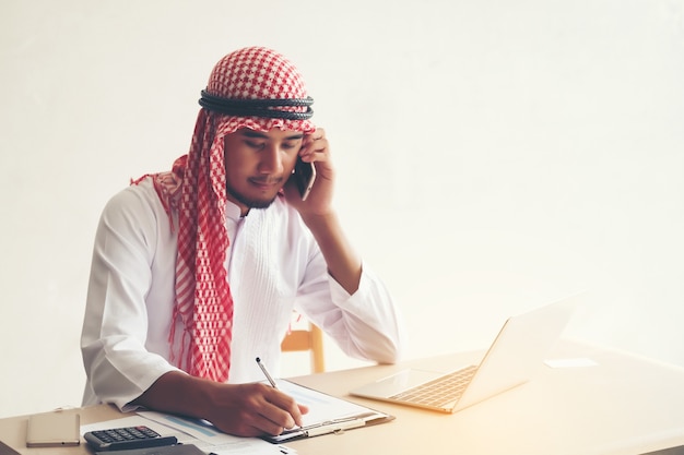 Árabe saudita homem trabalhando on-line com um laptop e chamando