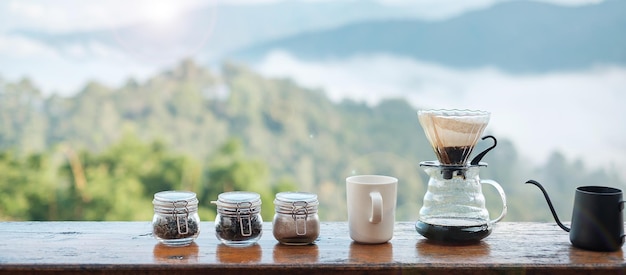 Arabica-Kaffeezubereitung mit Vintage-Kaffee-Tropfausrüstung, die morgens auf einem Holztisch mit Berg- und Naturhintergrund steht