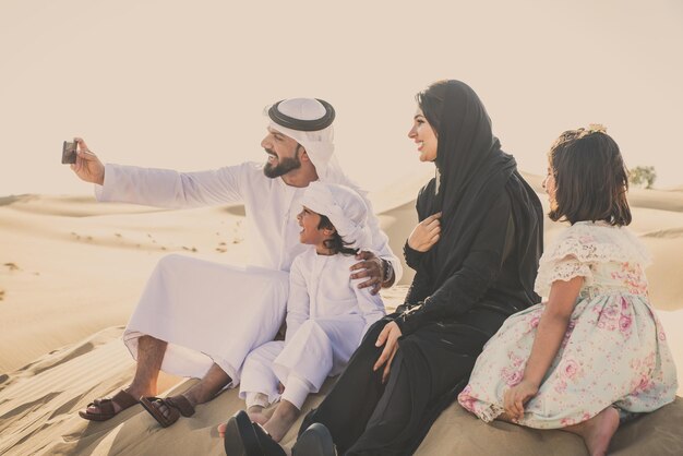 Arabische Familie macht ein Selfie, während sie in der Wüste gegen den Himmel sitzt