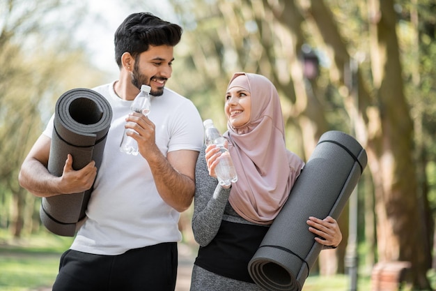 Arabische Familie mit Wasserflasche und Yogamatte im Park