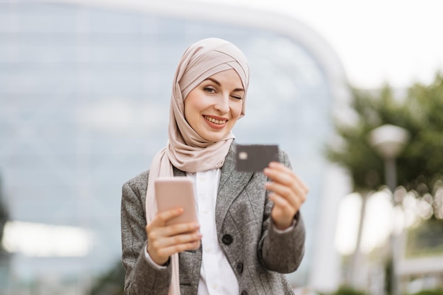 Arabische Frau mit Kopftuch auf der Straße mit Kaffee und Telefon zum Mitnehmen