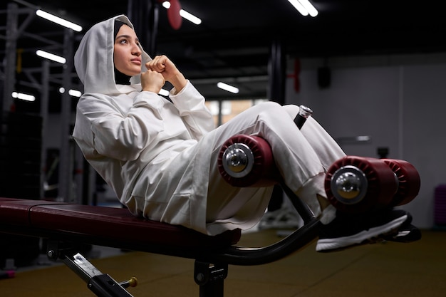 Arabische Frau pumpt Bauchmuskeln im Fitnesscenter, das auf Ausrüstung liegt, konzentriert auf Training, allein. Sport- und Crossfit-Konzept