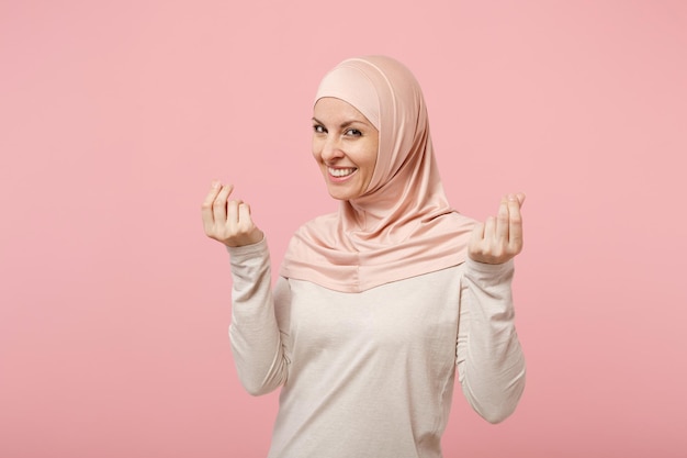 Arabische muslimische Frau in Hijab-leichter Kleidung, die isoliert auf rosafarbenem Hintergrund posiert. Menschen religiösen Islam Lifestyle-Konzept. Mock-up-Kopienbereich. Finger reiben, Geldgeste zeigen, um Geld bitten.