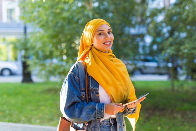 Arabische Studentin. Schöne muslimische Studentin, die leuchtend gelbe Hijab hält Tablette trägt.