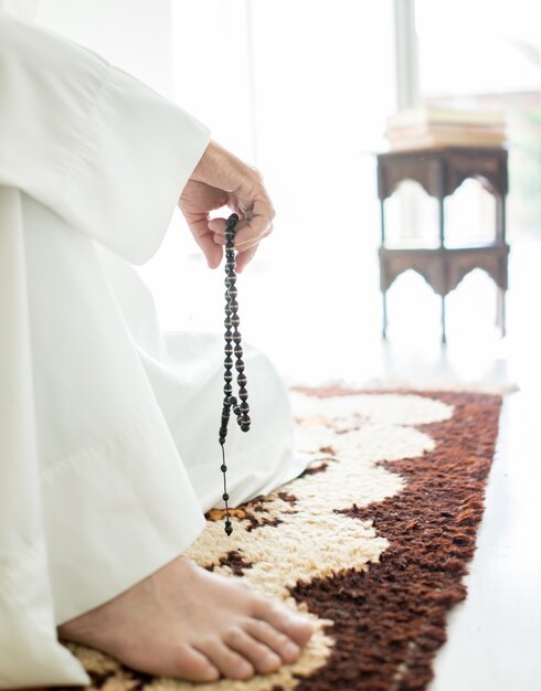 Arabischer gealterter Mann, der auf dem Boden unter Verwendung der traditionellen Perlen sitzt