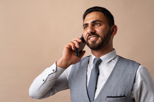 Arabischer Geschäftsmann, der auf seinem Handy vor beigem Hintergrund spricht