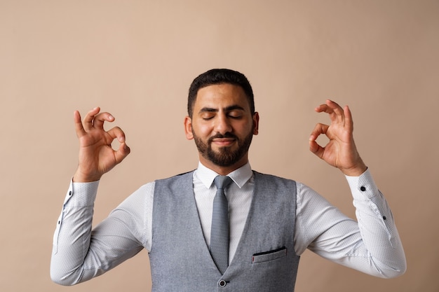 Arabischer Geschäftsmann, der in Zen-Pose steht und vor beigem Hintergrund meditiert