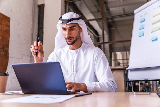 Arabischer Geschäftsmann mit traditioneller Kandura der Emirate bei der Arbeit in einem internationalen Unternehmen in Dubai?