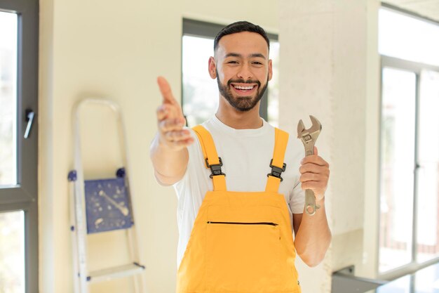 Foto arabischer gutaussehender mann arabischer mann lächelt glücklich und bietet oder zeigt ein konzept eines handwerkers mit einem schraubenschlüssel