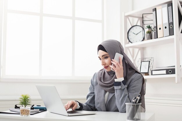 Arabischer Kundenvertreter, der im Büro am Laptop arbeitet und auf dem Handy berät