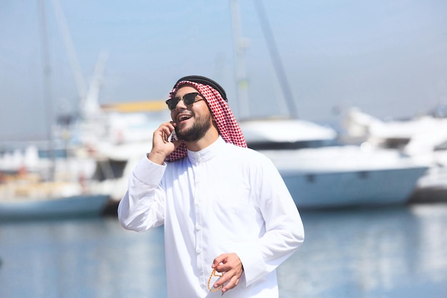 Arabischer Mann, der am Handy am Yachthafen spricht