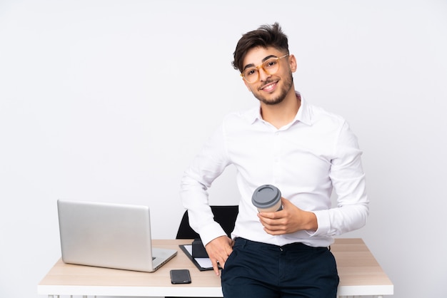 Arabischer Mann in einem Büro auf weißer Wand, die mit den Armen an der Hüfte aufwirft und lächelt