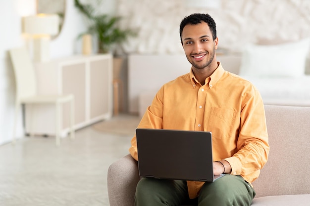 Arabischer Mann mit Laptop sitzt zu Hause auf der Couch