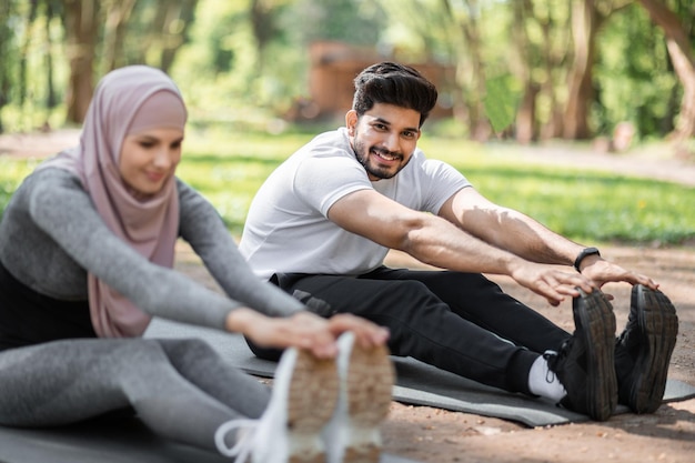 Arabischer Mann und Frau wärmen sich draußen auf einer Yogamatte auf