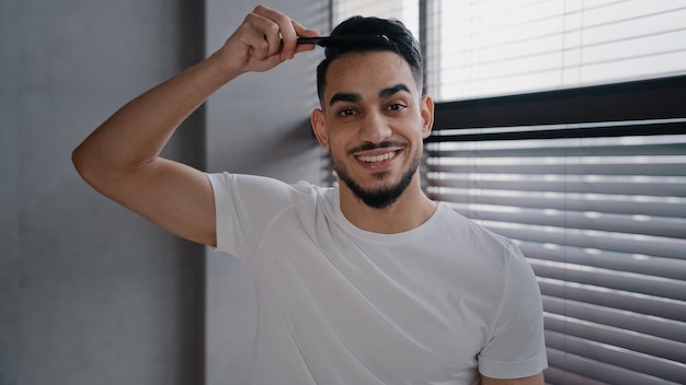 Arabischer Spanier, arabischer Mann, der in die Kamera blickt und Haare mit einer Haarbürste kämmt, um sich auf die Arbeit vorzubereiten