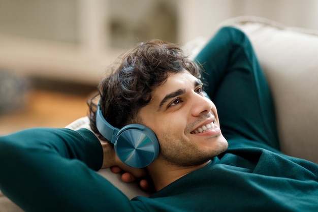 Arabischer Typ hört zu Hause mit Kopfhörern Musik auf der Couch