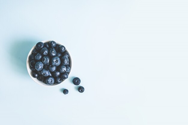 Arándano orgánico crudo fresco en una taza en superficie azul