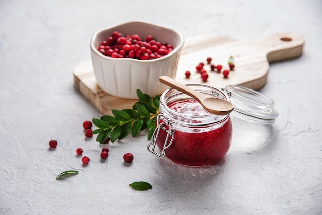 Arándano rojo del bosque jugoso con mermelada hecha a mano en un tazón sobre una mesa blanca y una tabla de cortar Concepto de comida saludable casera Cerrar y copiar la imagen del espacio