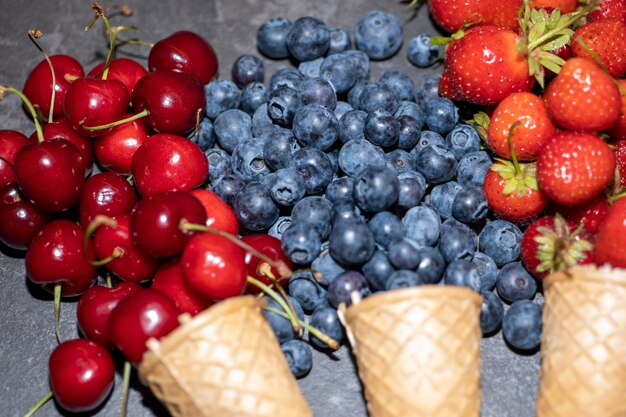 Arándanos, cerezas y fresas en tazas de gofres sobre un fondo oscuro