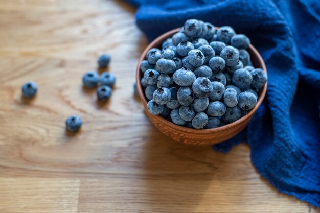 Arándanos en cuenco de arcilla con toalla azul sobre un fondo de madera cerrar