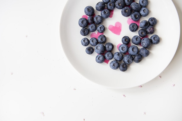 Arándanos deliciosos se encuentran en un plato con un corazón adentro. Comida deliciosa y saludable. Lugar para una inscripción.