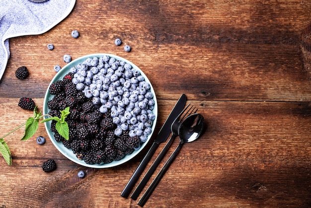 Arándanos y moras en un plato sobre un fondo de madera oscura con cubiertos. El concepto de vegetarianismo, comida sana.