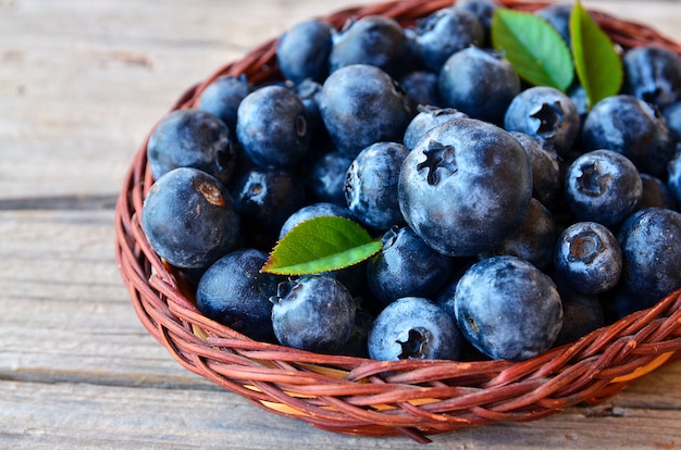 Arándanos recién recogidos en una cesta en la mesa de madera vieja. Arándanos frescos con hojas verdes en la mesa rústica. Arándano. Arándano. Concepto de alimentación saludable, dieta y nutrición.