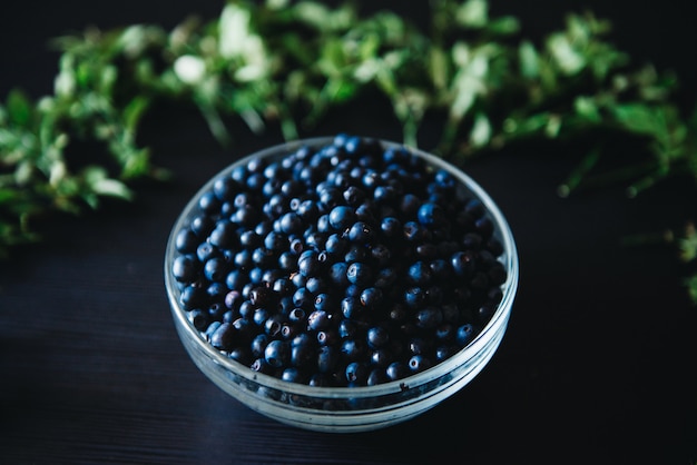 Arándanos en un recipiente de vidrio con ramitas y hojas sobre un fondo oscuro. Saludable comer fruta fresca de temporada.