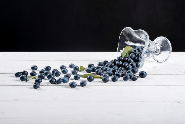 Arándanos sobre una mesa blanca con un fondo negro, la baya se esparce de la fruta de verano de vidrio