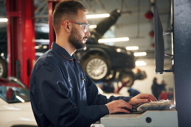 Arbeit am Computer Autoreparaturmann ist in der Garage mit Automobil