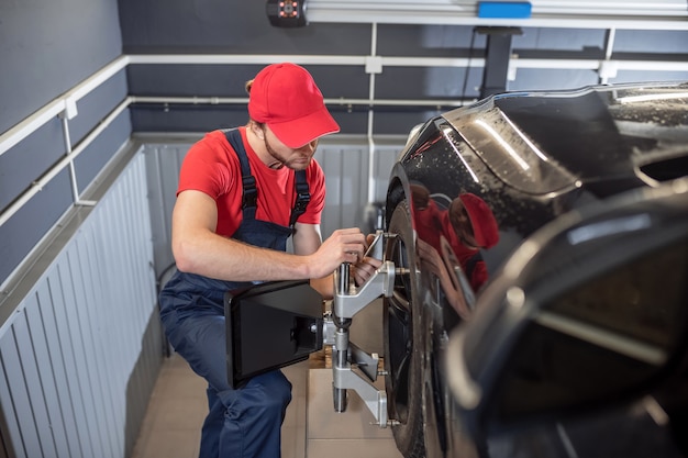 Arbeit, Automechaniker. Automechaniker in Overalls und roter Kappe, die nahe Rad des Autoreparaturdienstes stehen