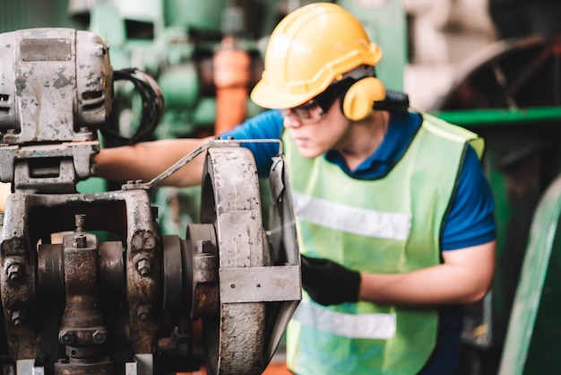 Arbeit in der Fabrik. Asiatischer Arbeiter, der in der Sicherheitsarbeit arbeitet, trägt mit gelbem Helm unter Verwendung der Maschine