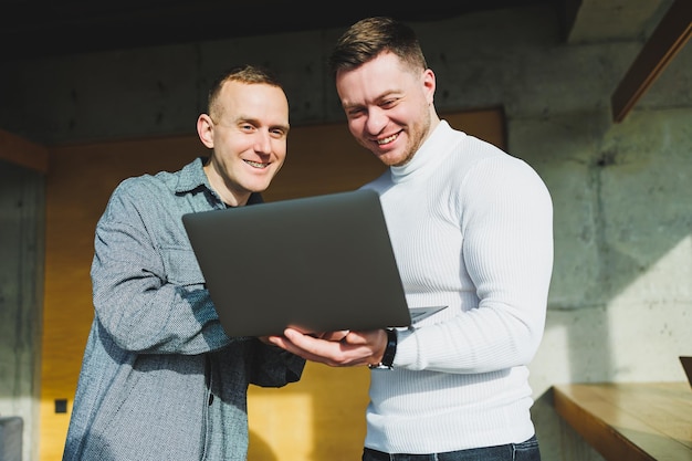 Arbeit von zwei männlichen Kollegen, die zusammen im Büro stehen, während sie Ideen mit Laptop im Besprechungsraum austauschen und Arbeitspläne analysieren Arbeiten Sie in einem modernen, geräumigen Büro