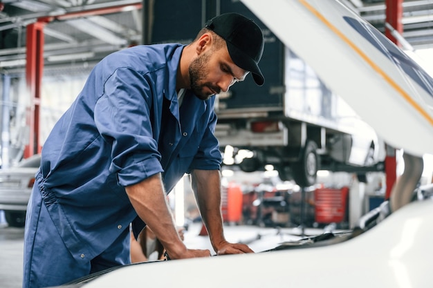Arbeiten an der Reparatur des Autos Die Motorhaube ist geöffnet Der Automechaniker ist in der Garage Reparaturdienst
