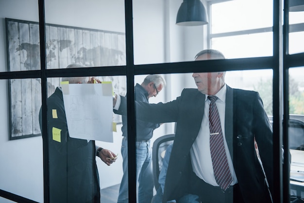 Arbeiten mit Aufklebern auf Glas. Ein gealtertes Team älterer Geschäftsmannarchitekten trifft sich im Büro.