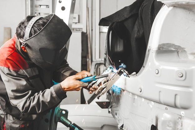 Arbeiten mit Kohlendioxidschweißen zur Reparatur von Metallkarosserien. Arbeiter bergen beschädigtes Auto. Schweißer bei der Arbeit