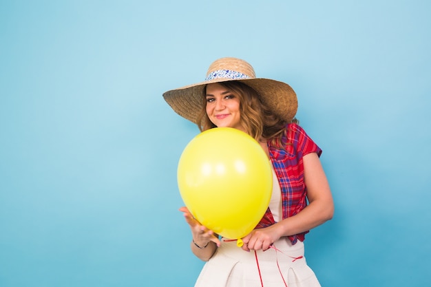 Arbeiten Sie lächelnde junge Frau mit gelbem Luftballon über buntem blauem Hintergrund mit Exemplar um.