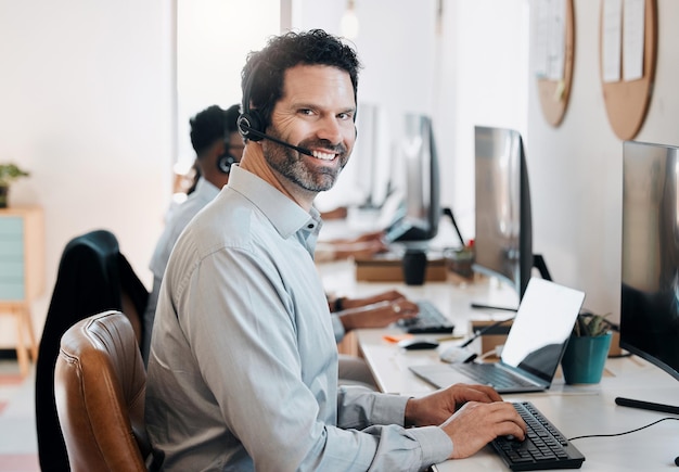 Arbeiten Sie so hart wie Ihr Team Aufnahme eines erwachsenen Agenten, der im Büro sitzt und seinen Computer benutzt, während seine Kollegen hinter ihm arbeiten