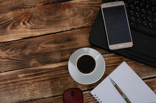 Arbeiten Sie vom Schreibtisch zu Hause aus mit Laptop, leerem Notizblock, Kaffeetasse und Stift auf Holztisch