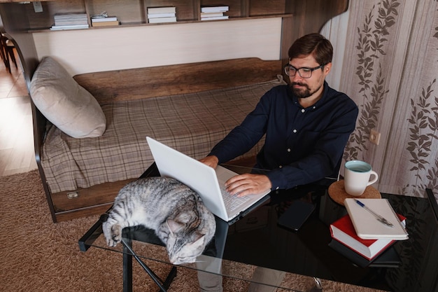 Arbeiten zu Hause mit Haustier auf dem Schoß Der Mensch arbeitet von zu Hause aus und tippt auf dem Laptop