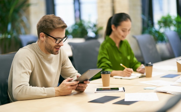 Arbeiten zusammen junger lächelnder kaukasischer Mann mit Brille mit digitalem Tablet beim Sitzen