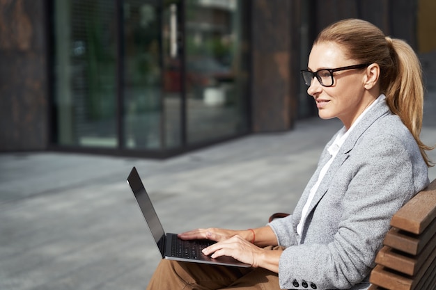 Arbeitende Online-Seitenansicht einer erfolgreichen Geschäftsfrau, die am Laptop arbeitet, während sie auf dem sitzt