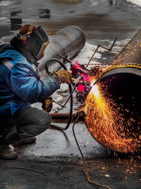 Arbeitender Schweißer schneidet Metall und Funken fliegen Gasschneiden von Rohren mit großem Durchmesser mit Acetylen und Sauerstoff Industrielles Metallschneiden in der Öl- und Gasindustrie
