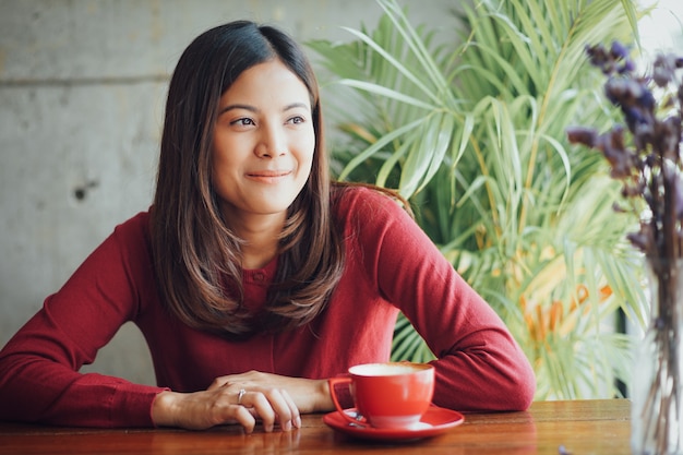 Arbeitender und trinkender Kaffee des asiatischen Geschäftsmädchens im Café mit Laptop