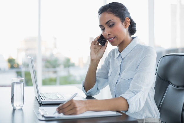 Arbeitendes Sitzen der schönen Geschäftsfrau an ihrem Schreibtisch