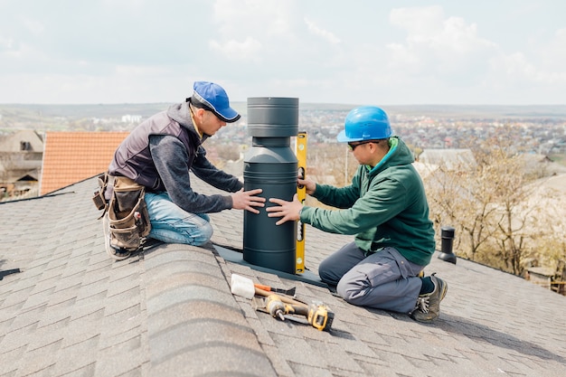 Arbeiter auf dem Dach, die Zinnkappe auf der Dachkonstruktion des eisernen Schornsteins installieren und ein neues Eisenhaus mit modularem Schornstein bauen
